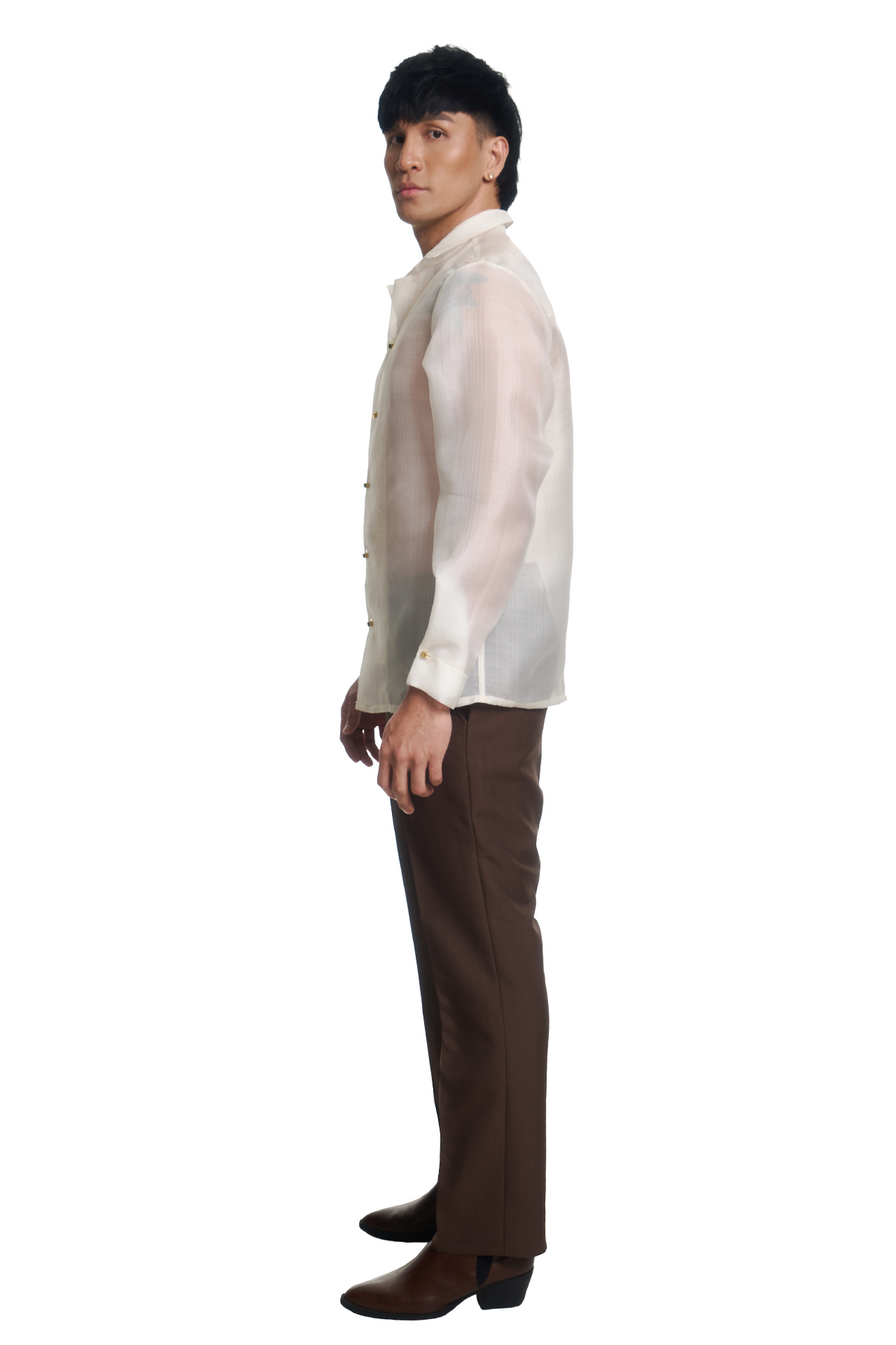 A man shown in full side profile wearing a white long-sleeve button-up shirt, brown trousers, and brown boots against a plain white studio background.