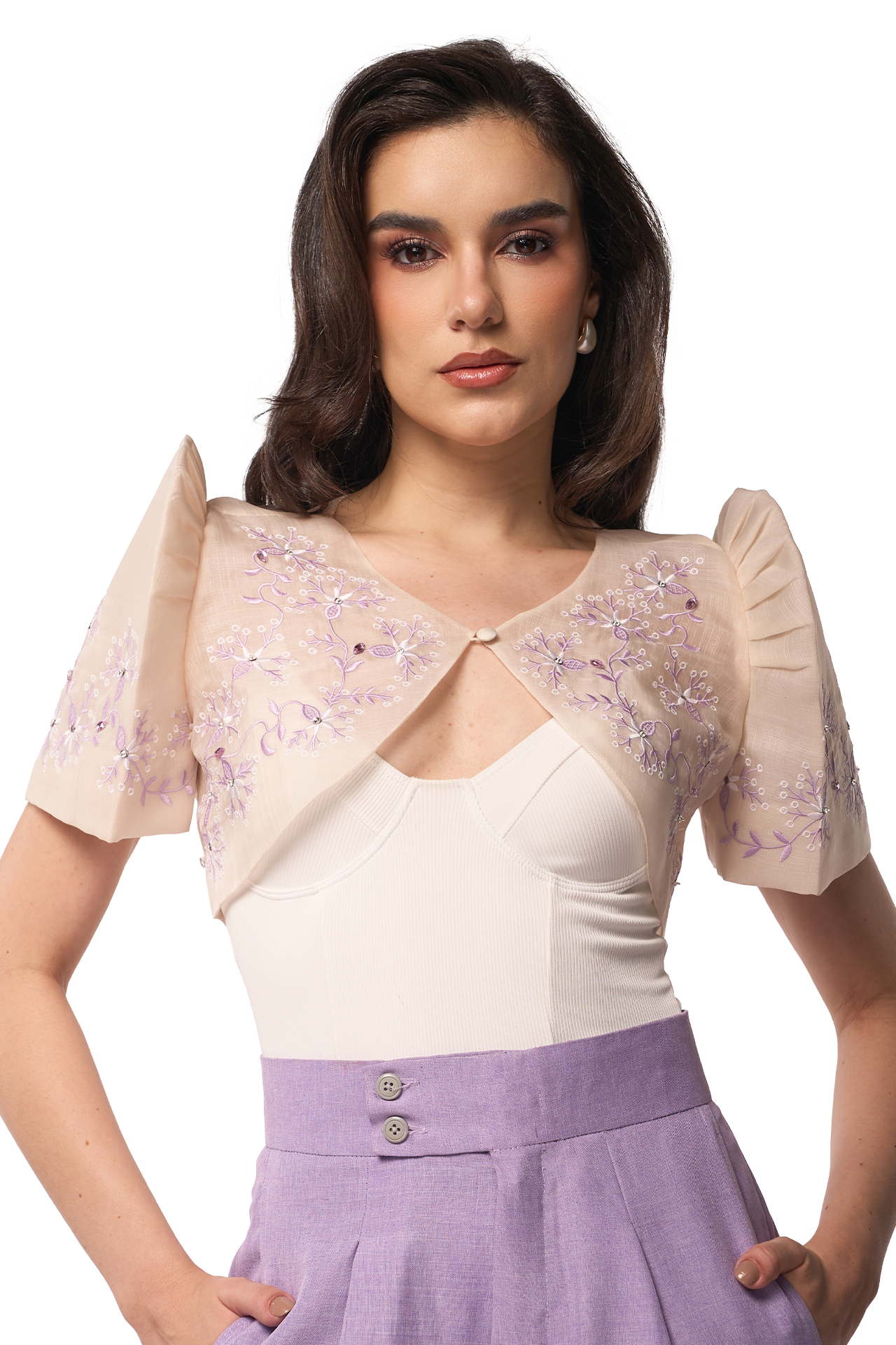 Woman wearing a beige embroidered shrug over a white top and purple skirt on a white background