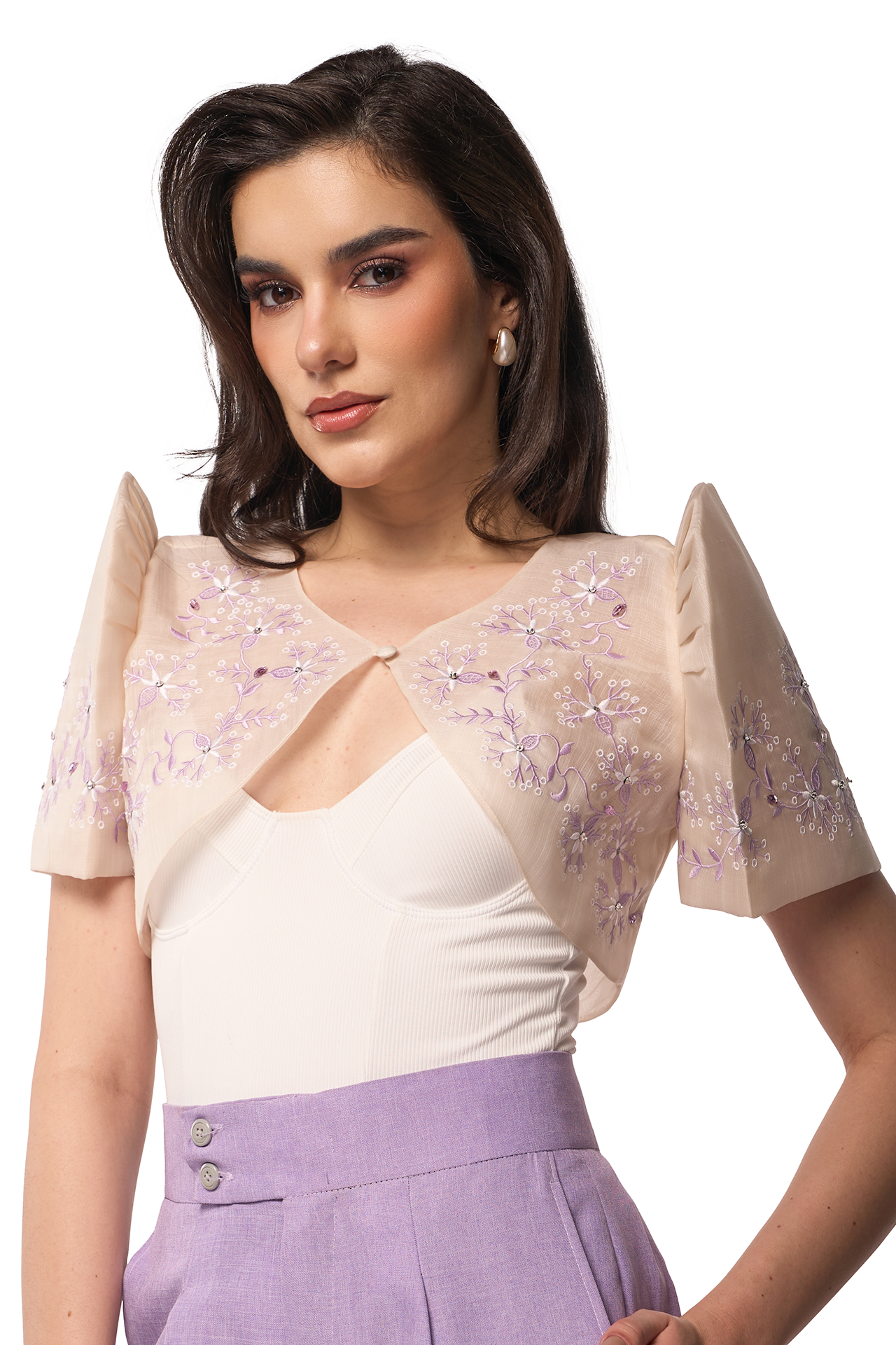 Woman wearing a beige top with floral embellishments and a white blouse underneath on a white background