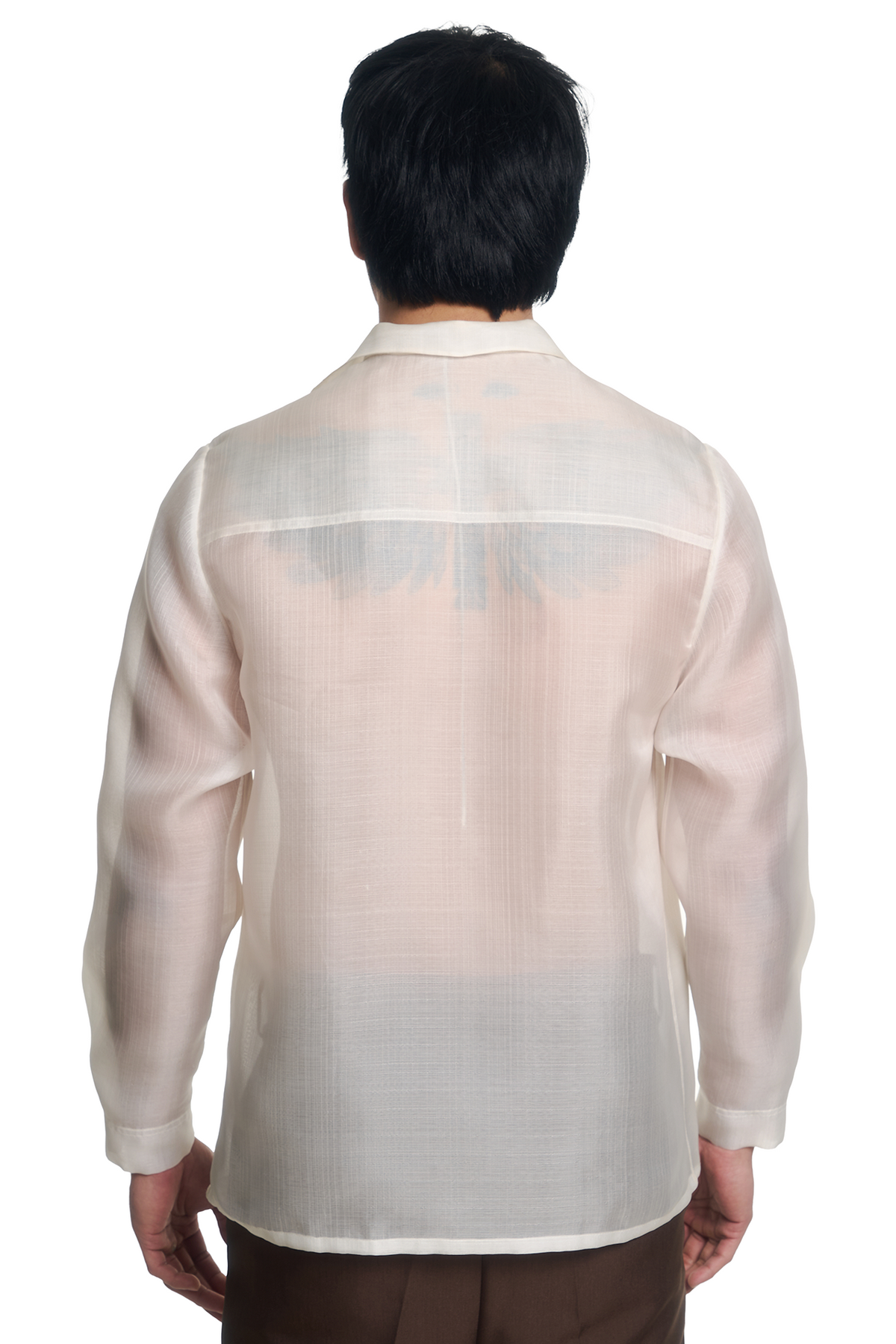 A man viewed from the back wearing a lightweight, semi-sheer barong in a warm off-white or cream color, paired with brown trousers against a solid white background.